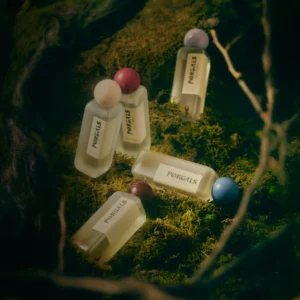Portals Parfums body spray bottles arranged on a moss-covered woodland setting.
