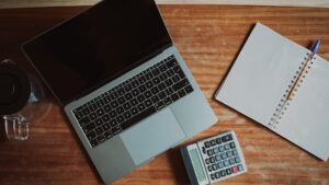 Laptop, calculator, and notebook arranged on a wooden desk