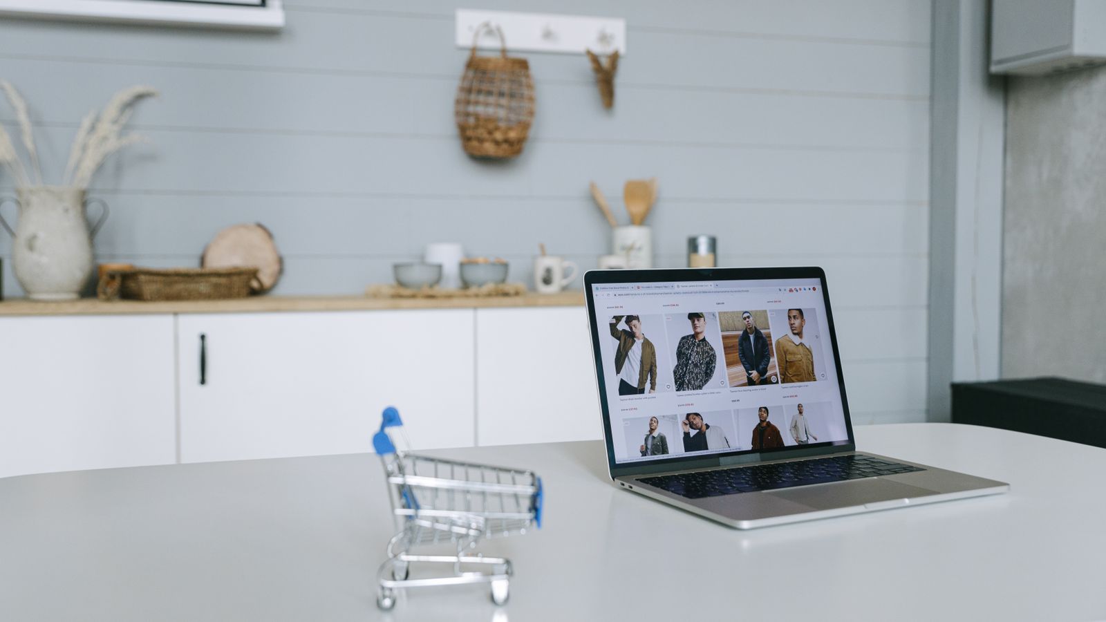 Laptop displaying an online store beside a miniature shopping cart.