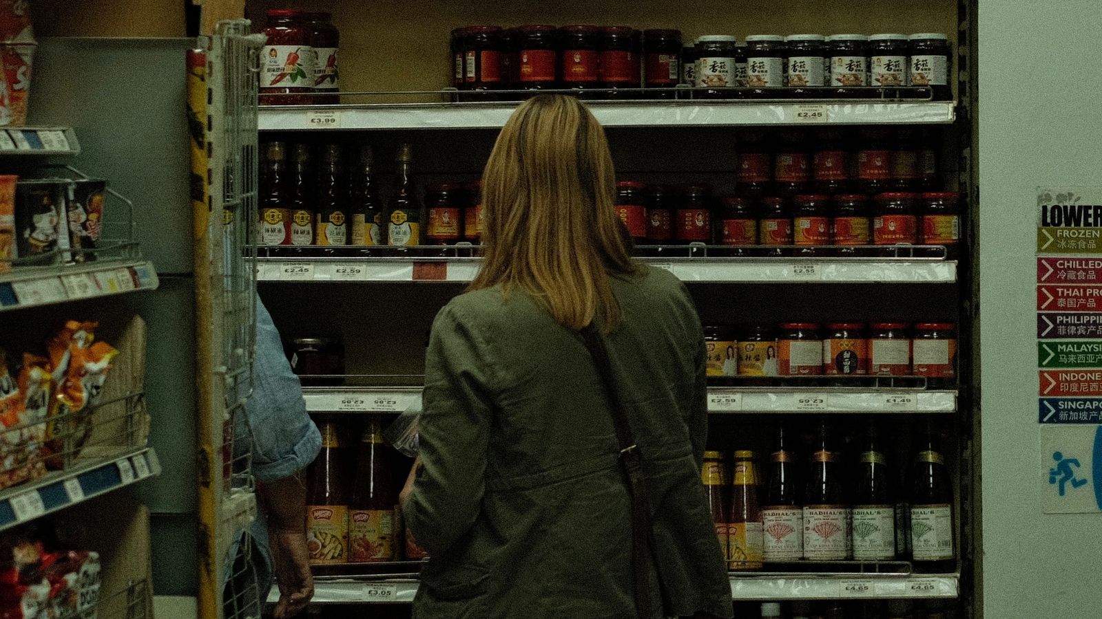 Shopper comparing products displayed on a store shelf.