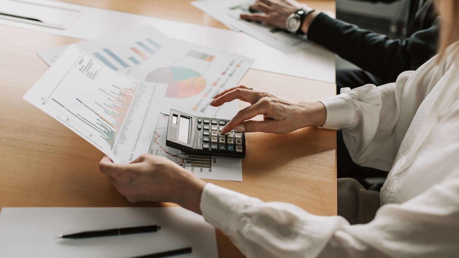 Hands reviewing financial charts with a calculator during a meeting.