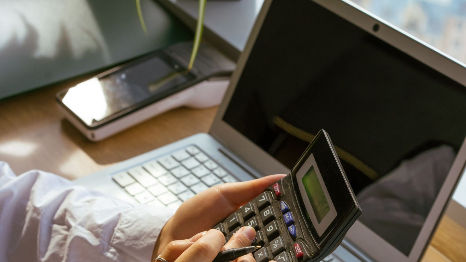Person calculating business costs beside a laptop and notebook.