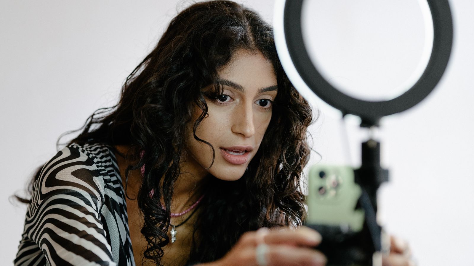 Creator adjusting a smartphone on a tripod with a ring light for product video production.